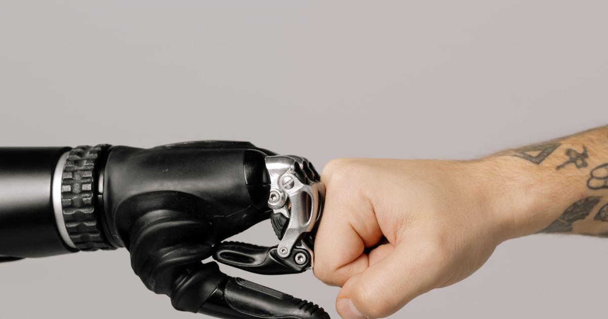 Close-up of a human fist punching a prosthetic hand, symbolizing technology and human connection.