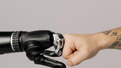 Close-up of a human fist punching a prosthetic hand, symbolizing technology and human connection.